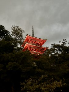 Auf dem Gelände des Kiyomizu-dera ragt zwischen den Bäumen die leuchtend rote dreistöckige Pagode hervor